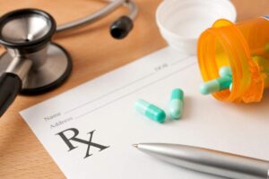 Two adults reading a medication label together at a kitchen counter, surrounded by medication bottles and a notepad.