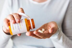 A person organizing medicine bottles on a high shelf away from a sunlit window in a home.